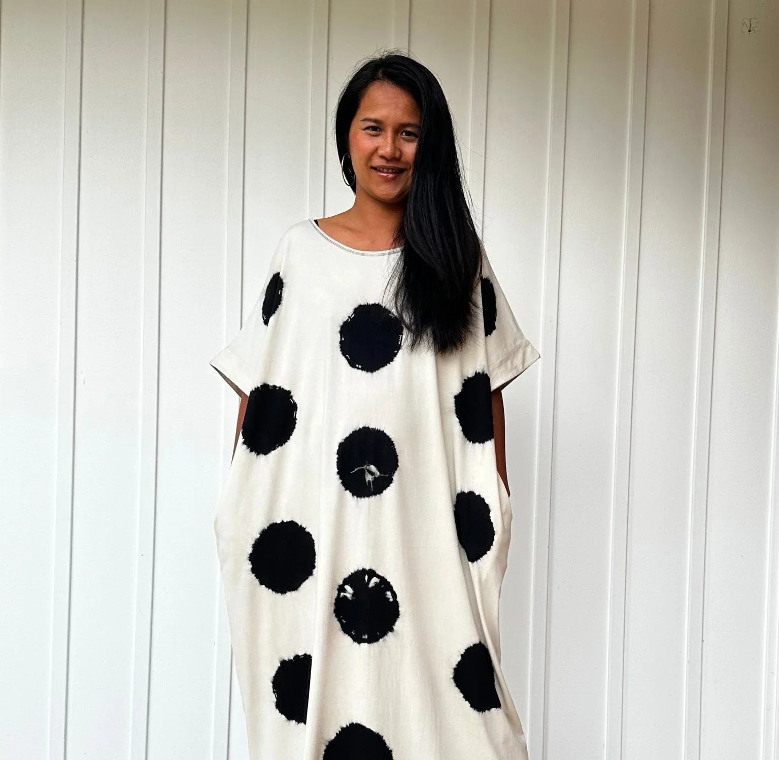 woman standing against white panel wall wearing white caftan with big black polka dots