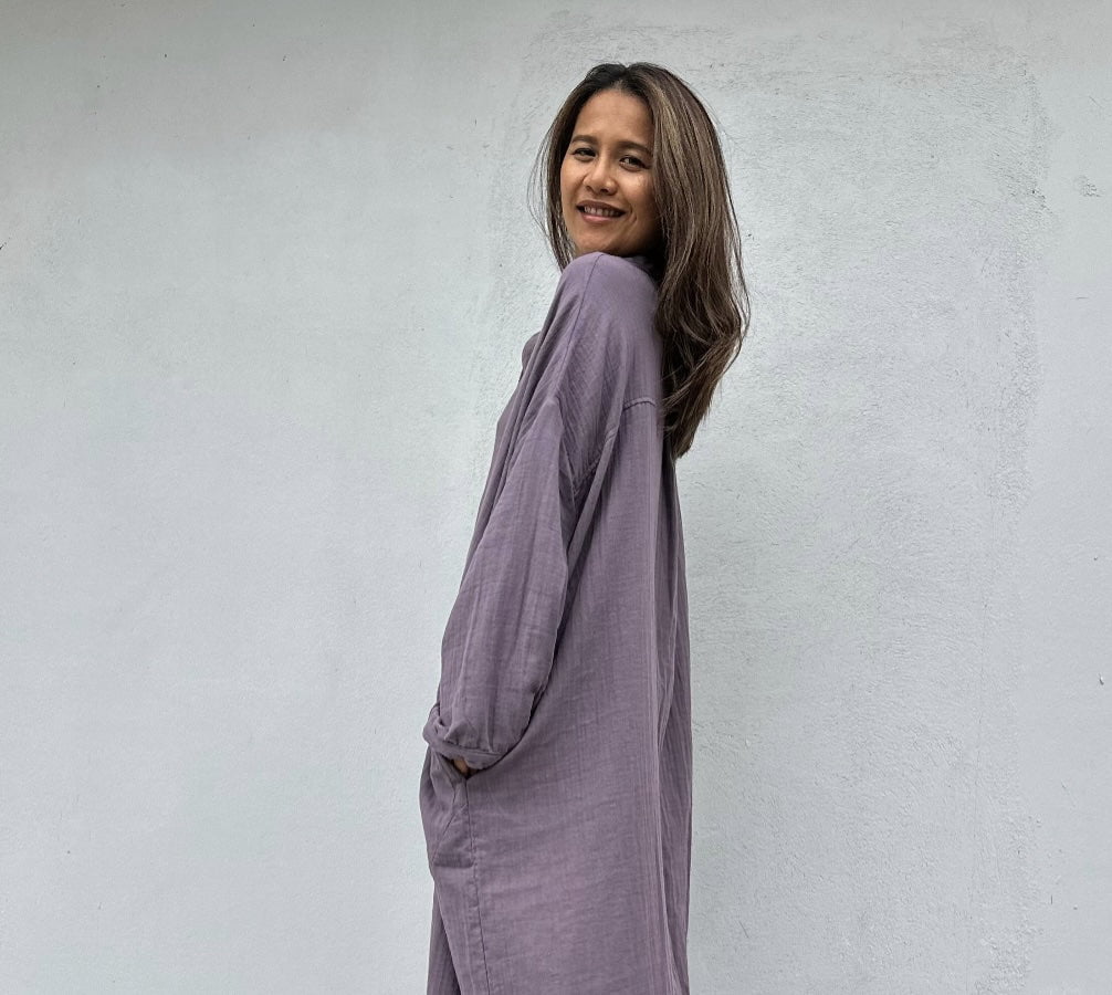 Woman wearing a long, light purple dress against a white wall