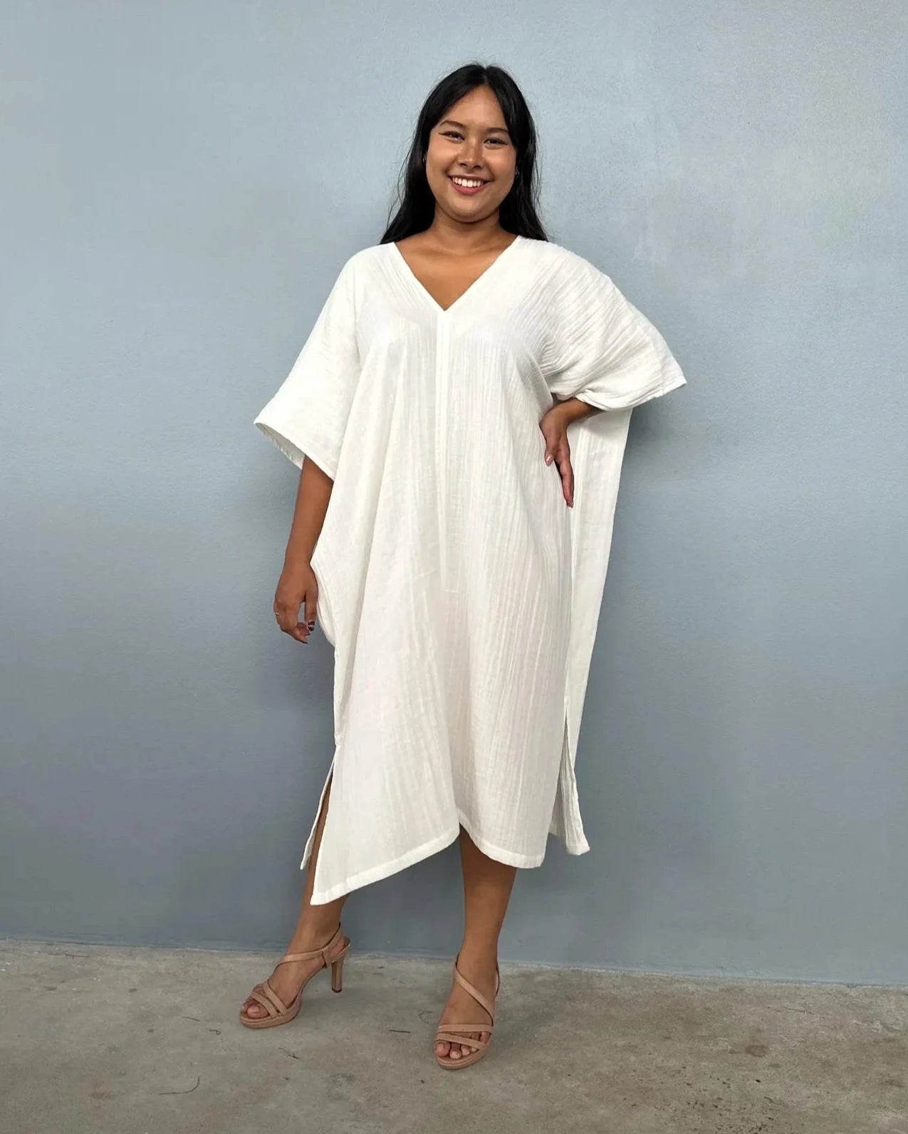 Woman wearing a white kaftan dress against a plain background