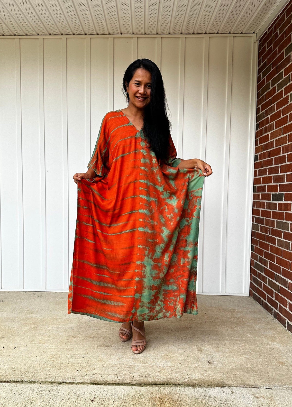 Woman wearing an orange and green dress standing on a porch.