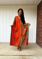 Woman wearing an orange and green dress standing on a porch.