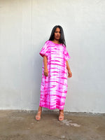 Woman wearing a pink tie-dye dress against a white wall.