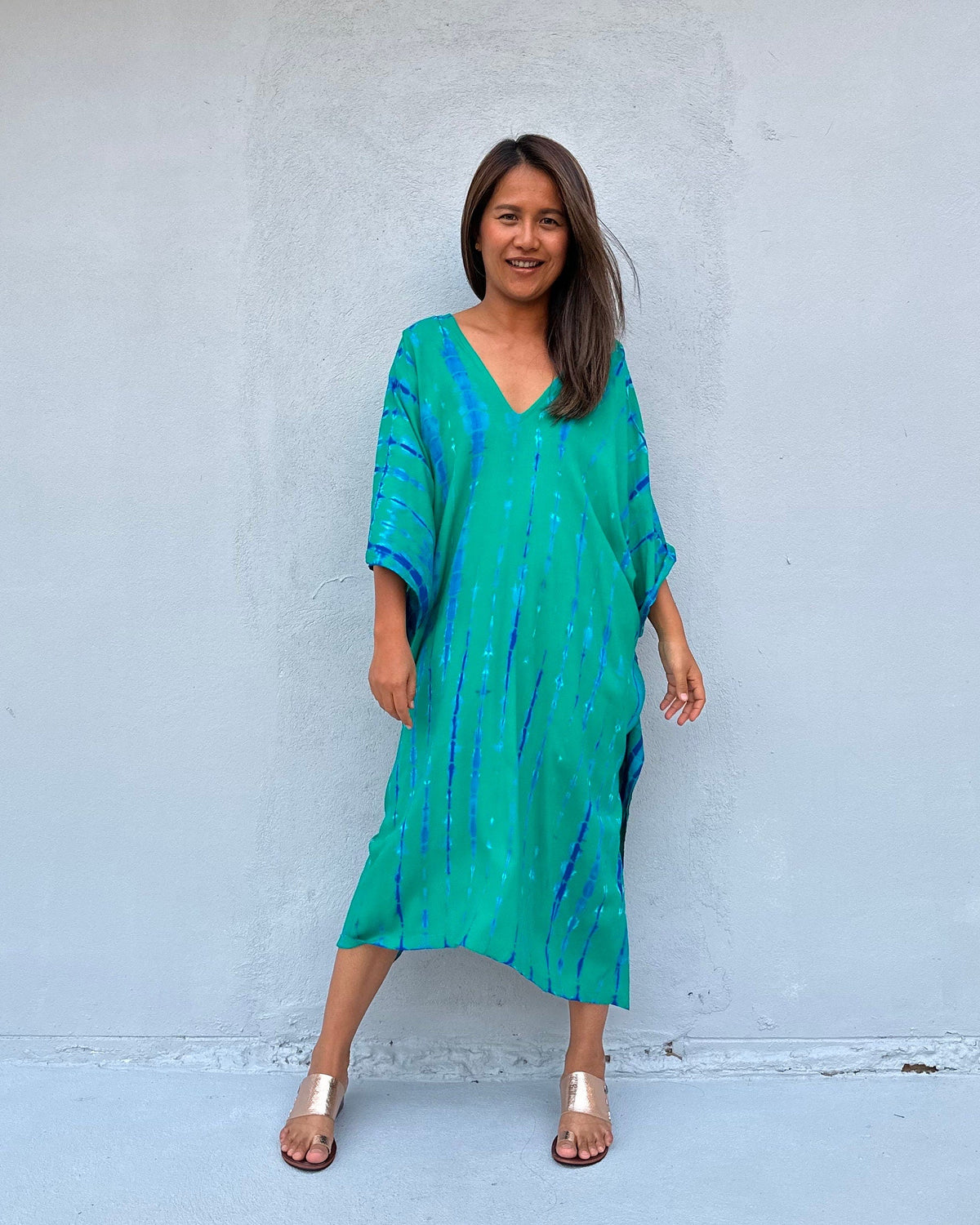 Woman wearing a green dress with blue patterns against a white wall
