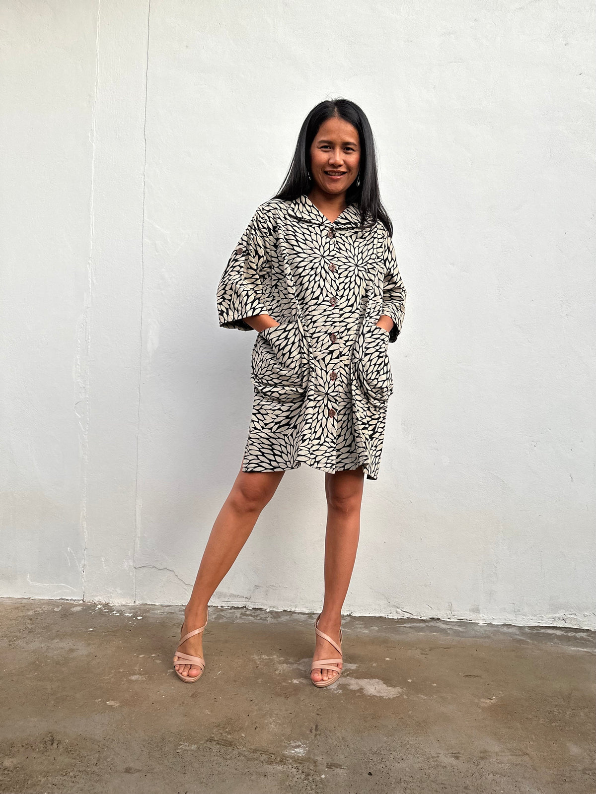A woman modeling a short-sleeve button-up shirt dress with a black and white abstract animal print, standing against a white wall.
