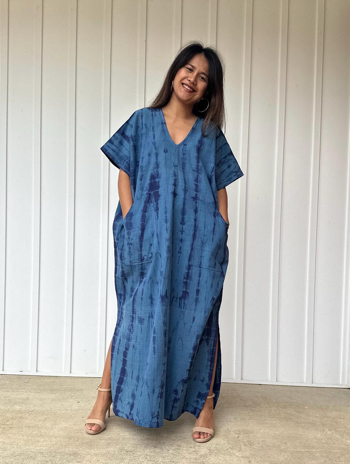 Woman wearing a blue tie-dye dress standing against a white paneled wall.