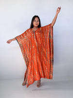 Woman wearing an orange tie-dye caftan against a white background
