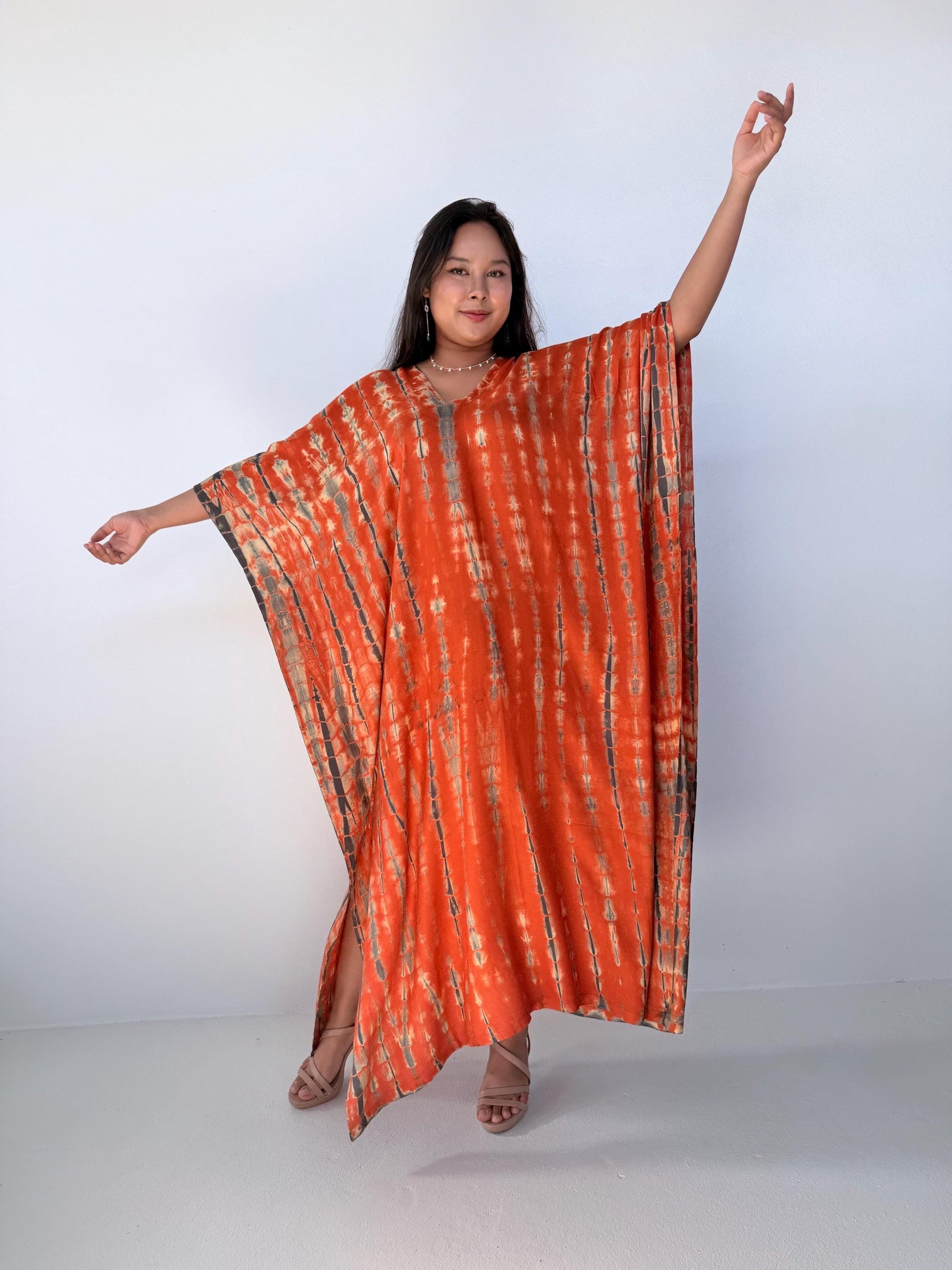 Woman wearing an orange tie-dye caftan against a white background