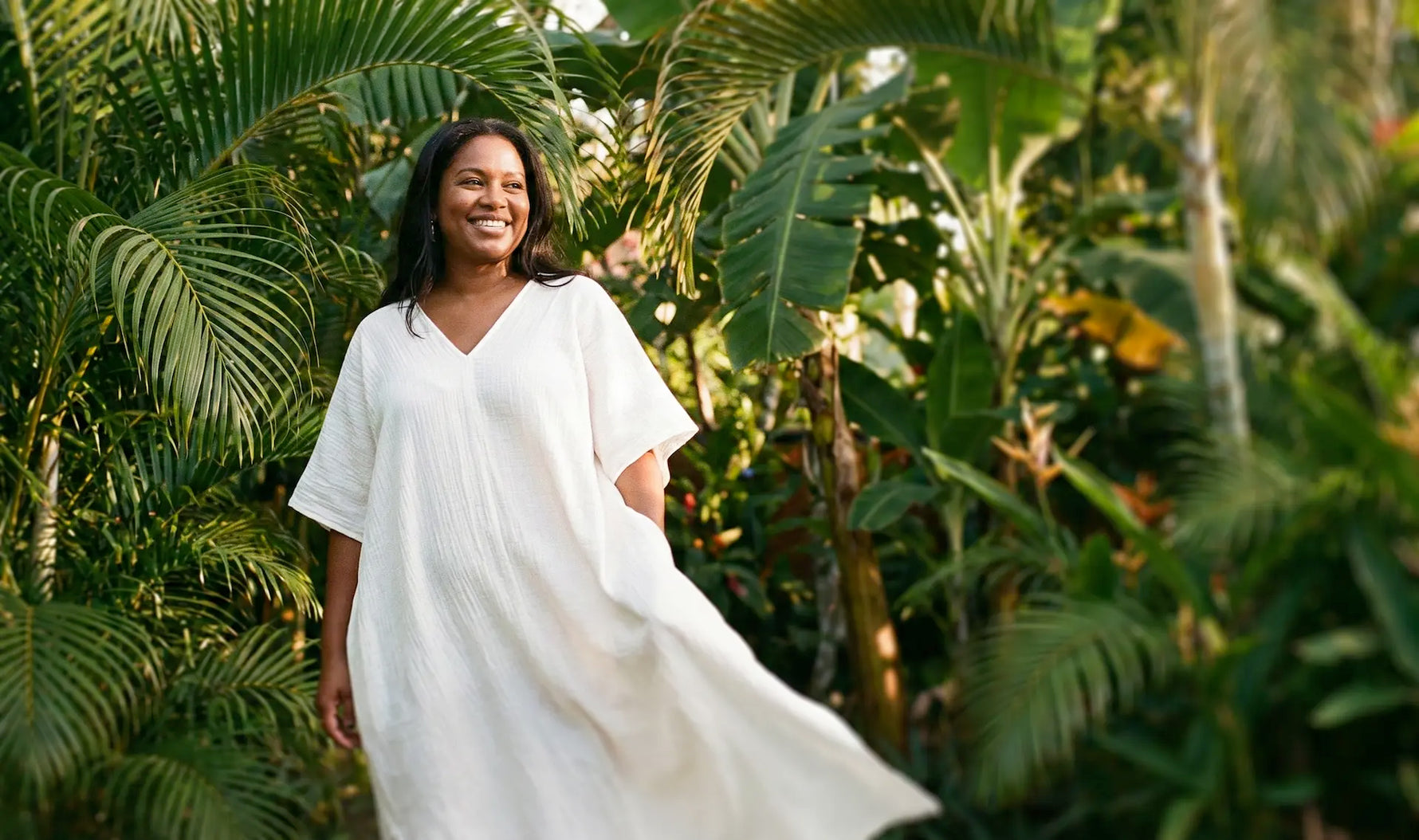 Woman in a white kaftan dress standing among tropical plants