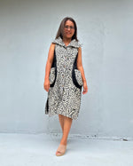 A woman modeling a sleeveless black and white patterned dress with black side pockets, standing against a light gray concrete wall.
