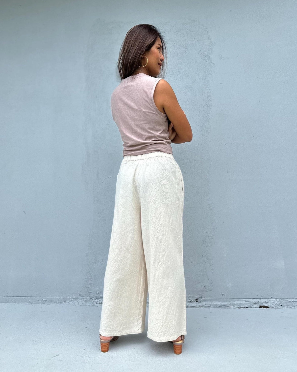 Person wearing a sleeveless top and wide-leg pants against a light blue wall.